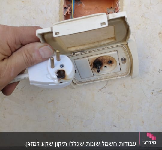 שקע חשמלי שרוף עם תקע פגום ביד אדם